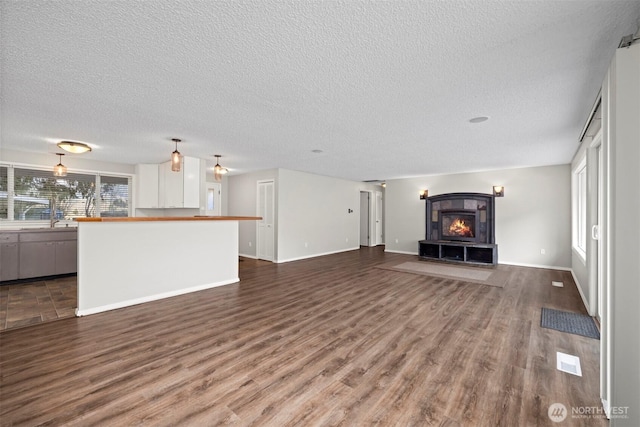 unfurnished living room with dark wood finished floors, a fireplace, a textured ceiling, and baseboards