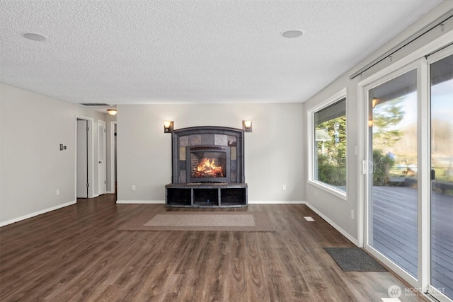 unfurnished living room with baseboards, a textured ceiling, wood finished floors, and a tile fireplace