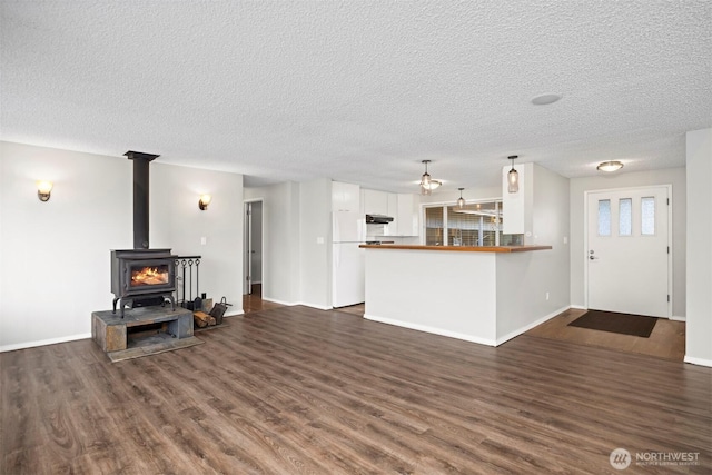 living room featuring a wood stove, baseboards, a textured ceiling, and dark wood-style flooring