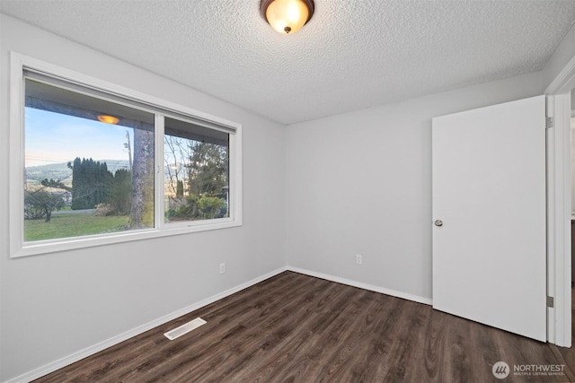 unfurnished room with dark wood-type flooring, baseboards, visible vents, and a textured ceiling