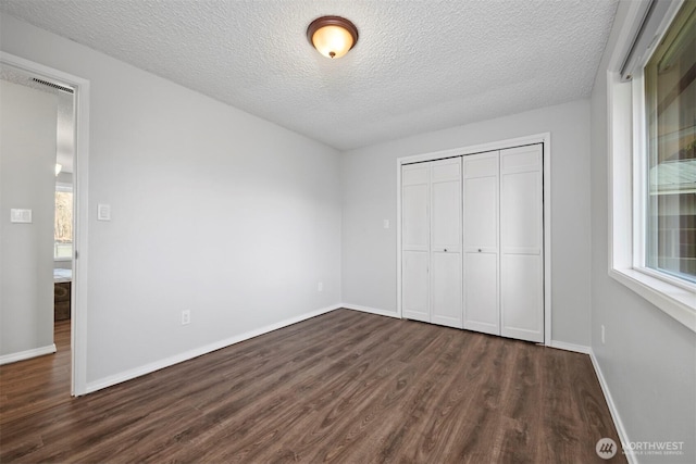 unfurnished bedroom featuring a closet, multiple windows, baseboards, and dark wood finished floors