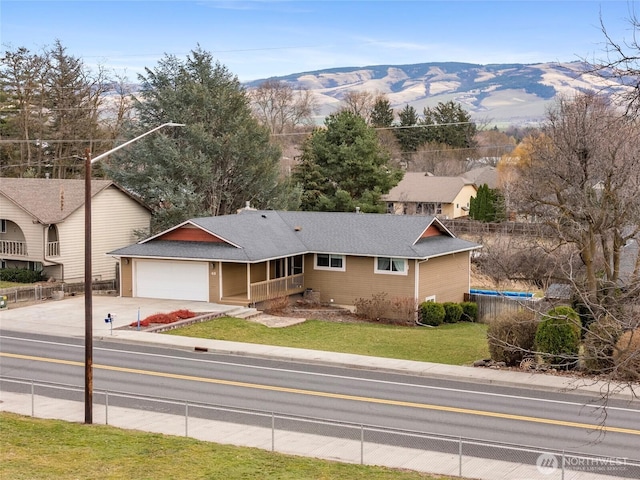 ranch-style house featuring driveway, a garage, fence, a mountain view, and a front lawn