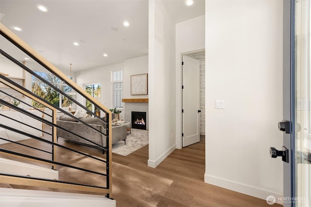 staircase with recessed lighting, a warm lit fireplace, baseboards, and wood finished floors