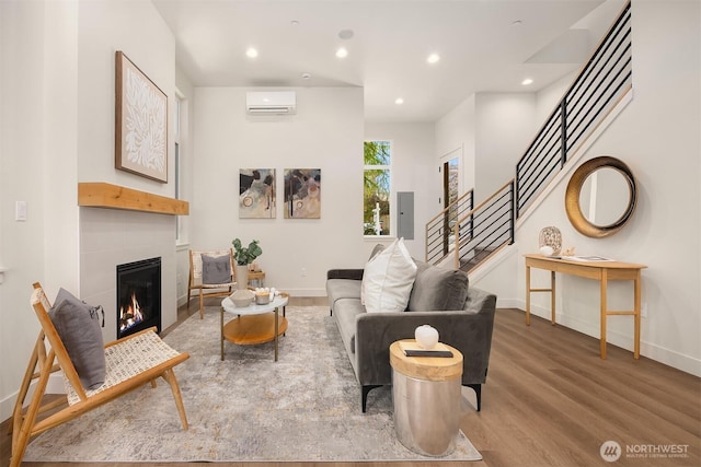 living area featuring baseboards, a tiled fireplace, stairway, wood finished floors, and an AC wall unit