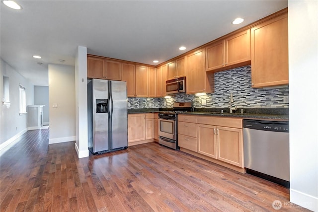 kitchen with a sink, backsplash, dark wood-style floors, appliances with stainless steel finishes, and baseboards