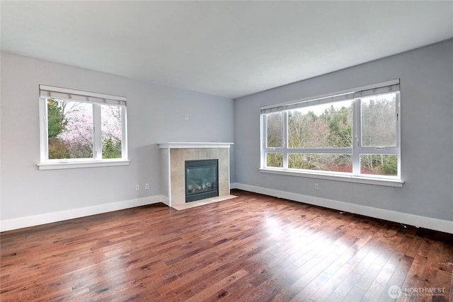 unfurnished living room featuring a fireplace, wood finished floors, baseboards, and a wealth of natural light