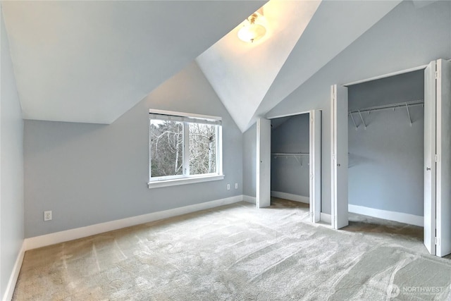 unfurnished bedroom featuring carpet flooring, two closets, baseboards, and vaulted ceiling