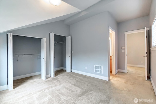 unfurnished bedroom featuring visible vents, two closets, baseboards, carpet, and lofted ceiling