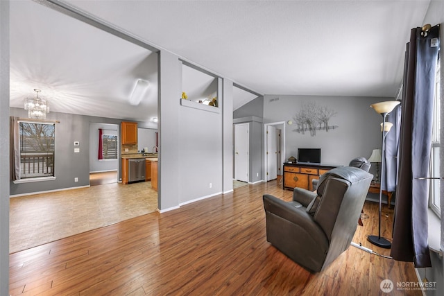 living room with lofted ceiling, light wood finished floors, baseboards, and a notable chandelier