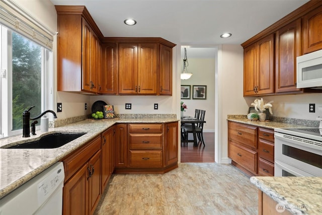 kitchen with brown cabinets, white appliances, a sink, and light stone countertops