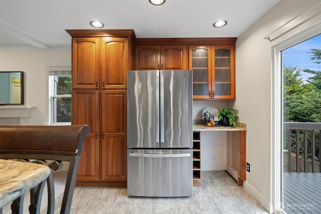 kitchen with light stone counters, glass insert cabinets, plenty of natural light, and freestanding refrigerator