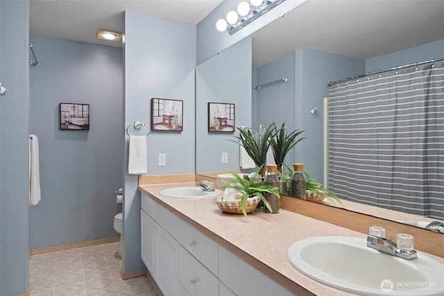 bathroom featuring double vanity, a sink, toilet, and baseboards