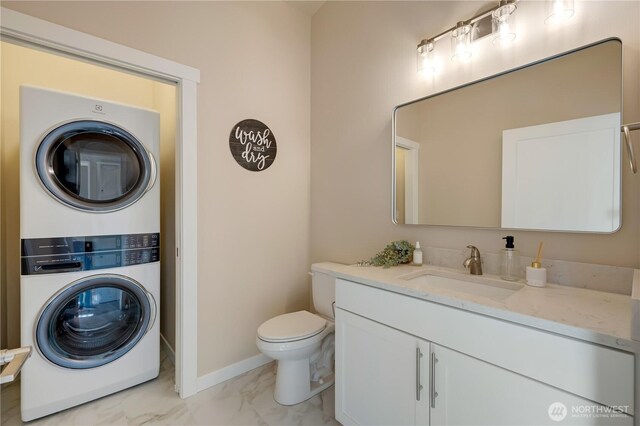 bathroom with toilet, stacked washer / dryer, vanity, baseboards, and marble finish floor