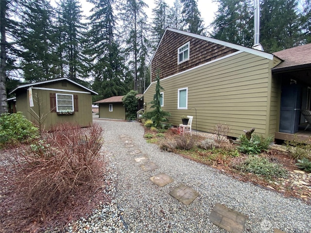 view of side of property with gravel driveway, roof with shingles, and an outdoor structure