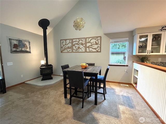 carpeted dining area with high vaulted ceiling, a wood stove, and baseboards