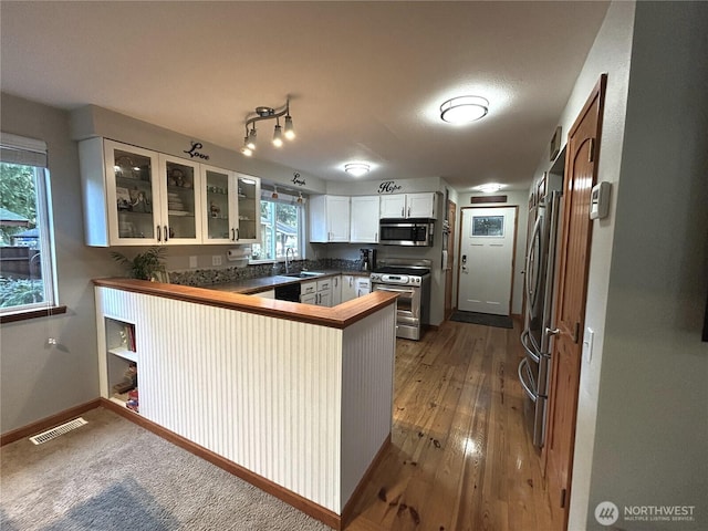 kitchen featuring visible vents, glass insert cabinets, a peninsula, stainless steel appliances, and a sink