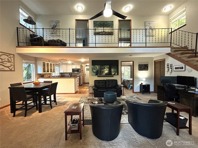 living room featuring a ceiling fan, baseboards, light colored carpet, and a high ceiling