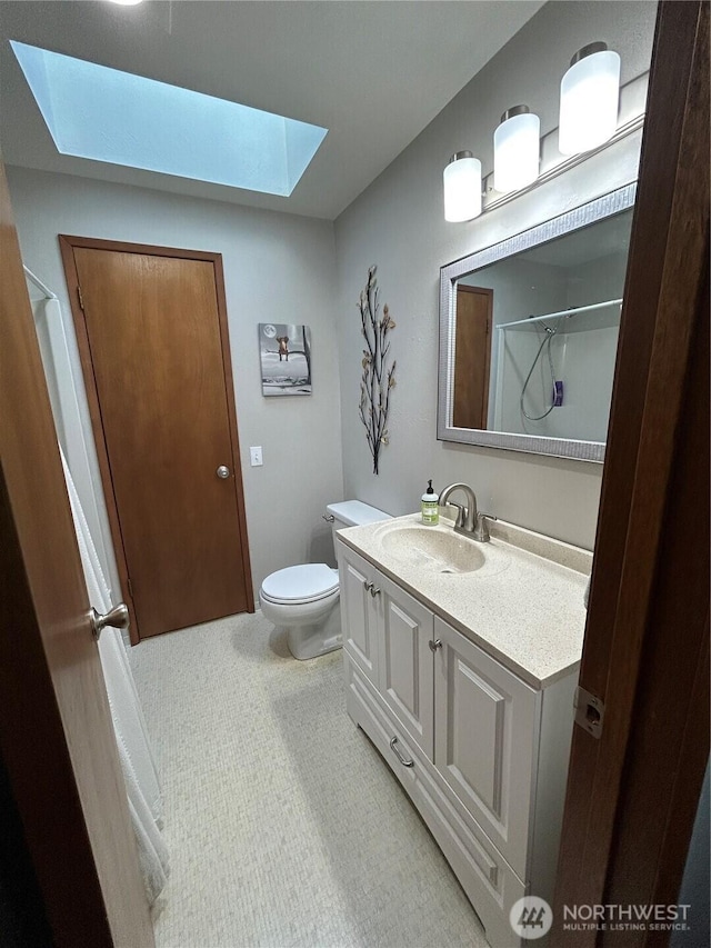 bathroom featuring toilet, a skylight, a shower, and vanity