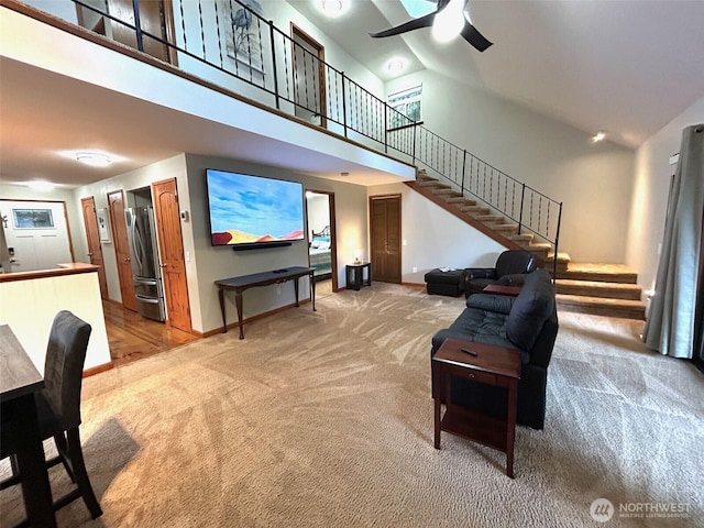 living area featuring a high ceiling, a ceiling fan, carpet flooring, baseboards, and stairs