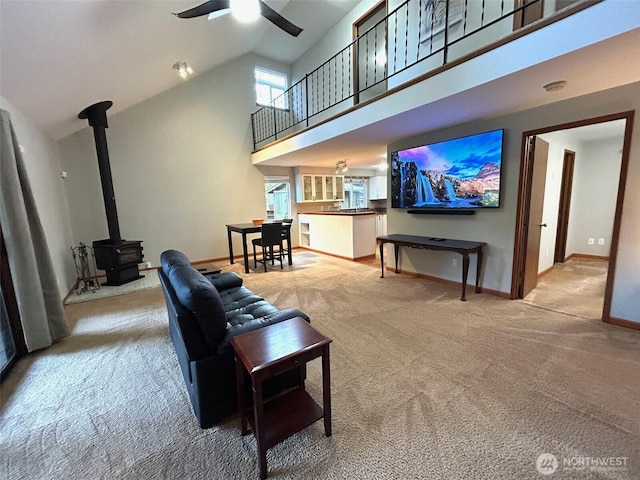 carpeted living room featuring a wood stove, high vaulted ceiling, baseboards, and a ceiling fan