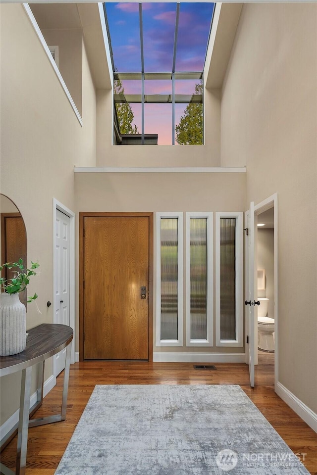 entrance foyer featuring visible vents, baseboards, wood finished floors, and a towering ceiling