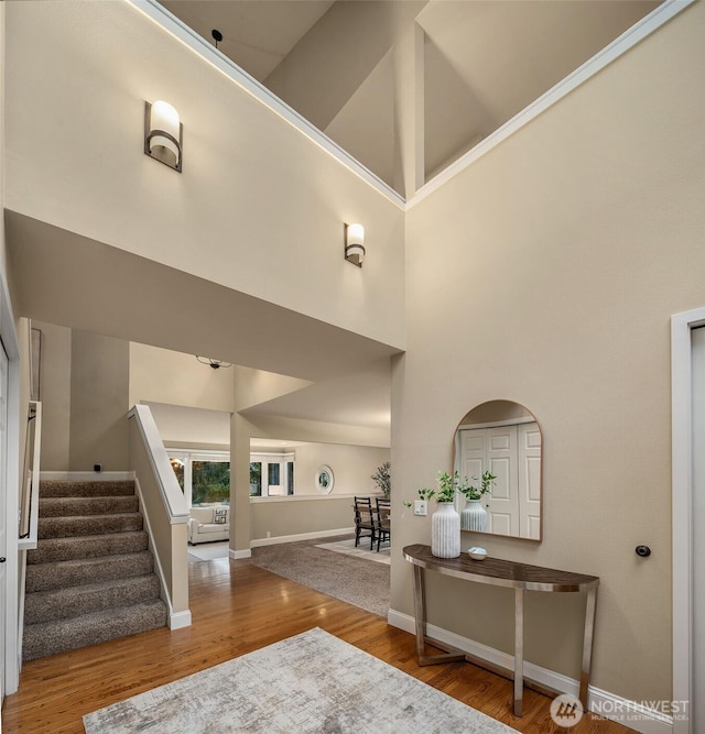 entryway featuring baseboards, a high ceiling, wood finished floors, and stairs