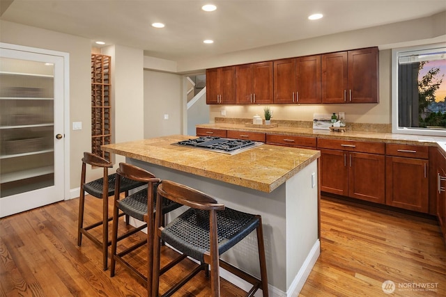 kitchen with a breakfast bar, a center island, recessed lighting, stainless steel gas stovetop, and light wood finished floors