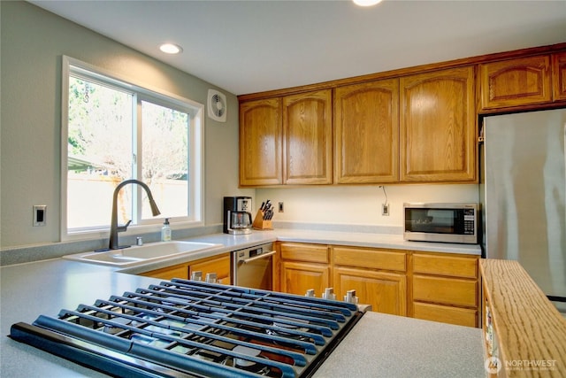 kitchen featuring light countertops, recessed lighting, brown cabinetry, stainless steel appliances, and a sink