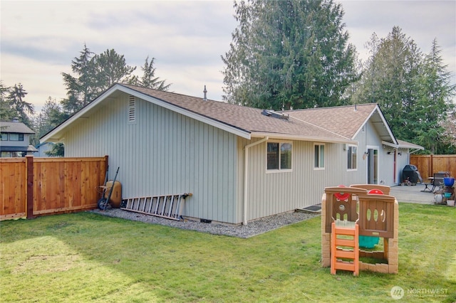 exterior space featuring a patio area, a lawn, a shingled roof, and fence