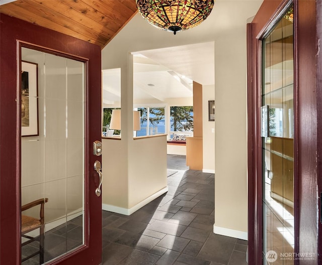 hall featuring stone finish floor, wood ceiling, baseboards, and vaulted ceiling