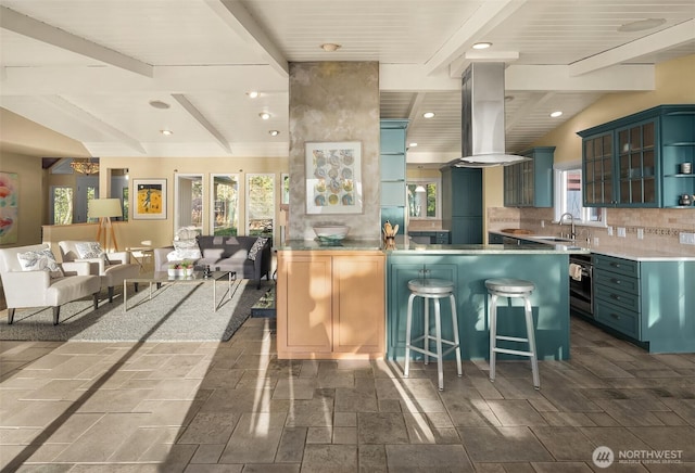 kitchen featuring a breakfast bar, vaulted ceiling with beams, island exhaust hood, backsplash, and a sink