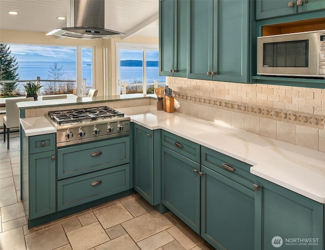 kitchen featuring exhaust hood, green cabinets, light countertops, appliances with stainless steel finishes, and backsplash