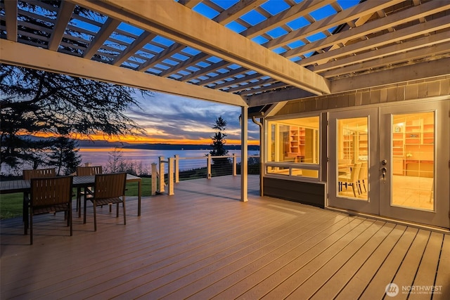 deck at dusk featuring a water view and a pergola