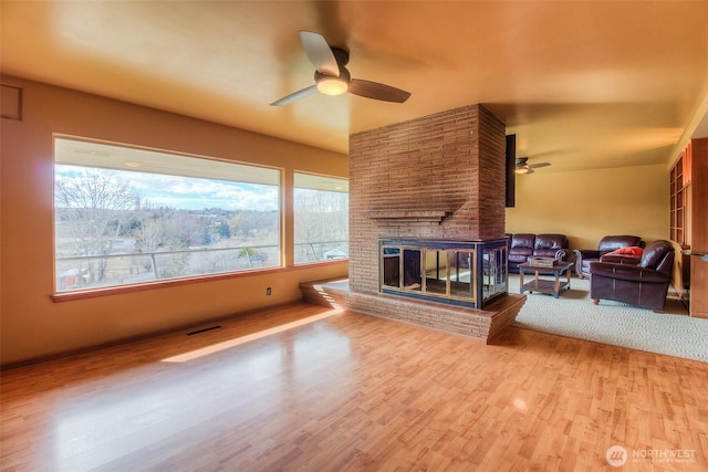 living room with visible vents, baseboards, ceiling fan, wood finished floors, and a brick fireplace