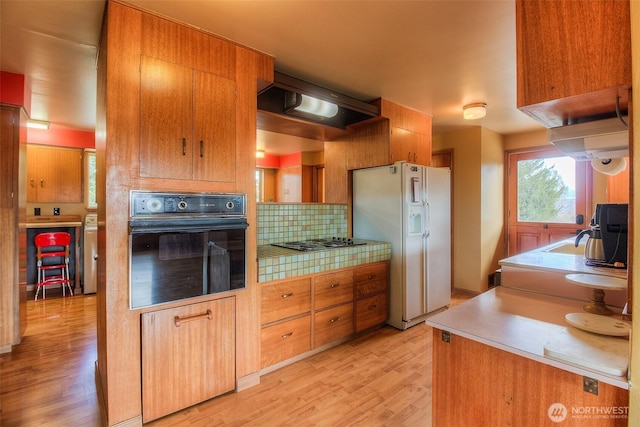 kitchen with white refrigerator with ice dispenser, stainless steel gas stovetop, decorative backsplash, light wood-type flooring, and black oven