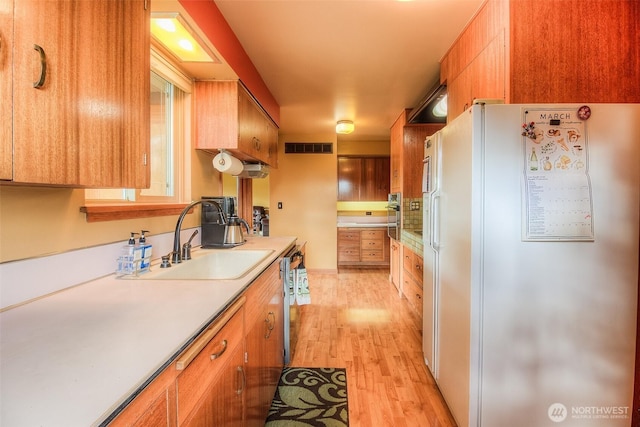 kitchen with light countertops, visible vents, light wood-style floors, freestanding refrigerator, and a sink