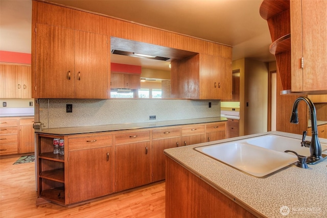 kitchen with light wood finished floors, tasteful backsplash, open shelves, and a sink