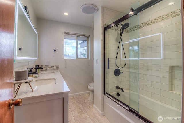 bathroom with double vanity, toilet, combined bath / shower with glass door, a sink, and baseboards