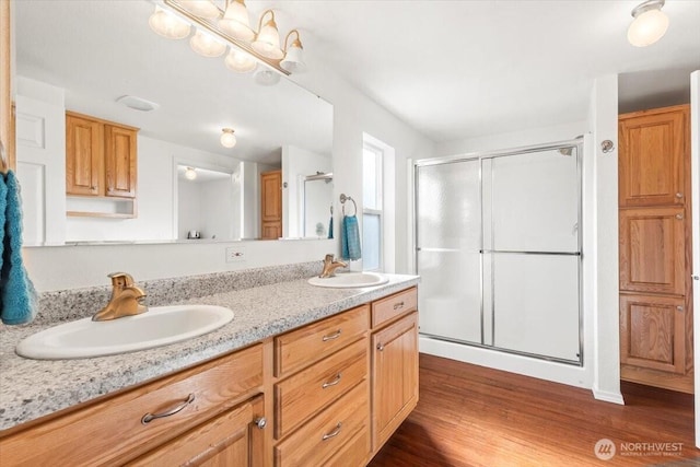 full bathroom with a stall shower, double vanity, a sink, and wood finished floors