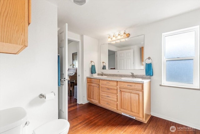 full bathroom with toilet, wood finished floors, a sink, baseboards, and double vanity