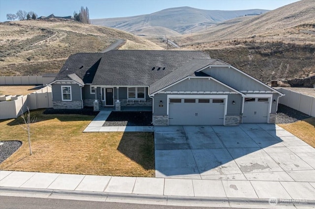 craftsman-style home featuring an attached garage, stone siding, fence, and a front yard