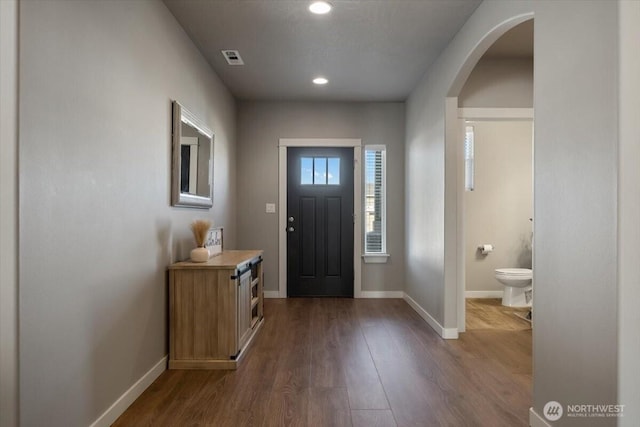 entrance foyer featuring baseboards, visible vents, arched walkways, and dark wood-type flooring