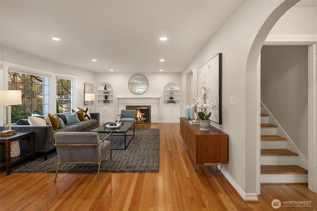 living area featuring built in shelves, light wood-style flooring, recessed lighting, a fireplace, and stairs