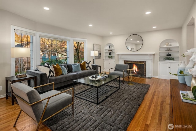 living area with built in features, recessed lighting, a brick fireplace, and wood finished floors