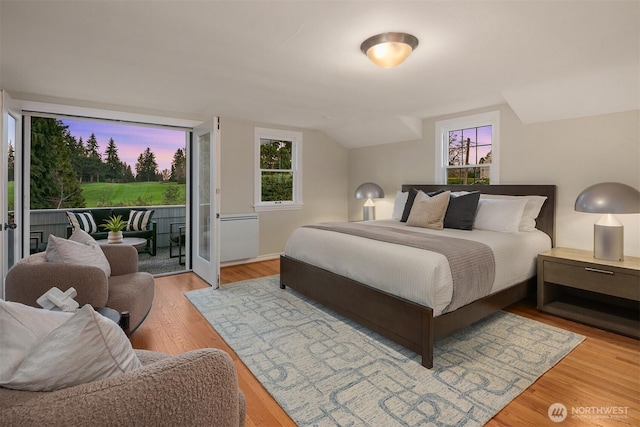 bedroom with access to exterior, light wood-style floors, and vaulted ceiling