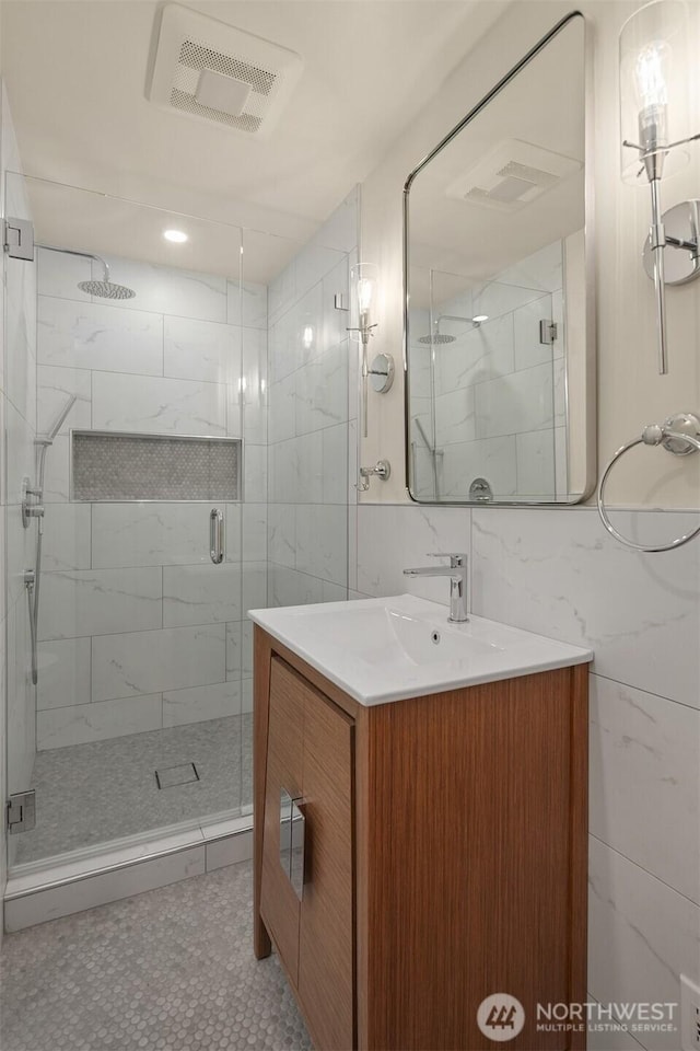 bathroom with visible vents, vanity, tile walls, and a shower stall