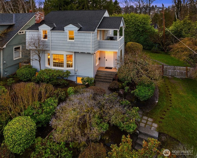 view of front of house with a front yard, a balcony, and roof with shingles