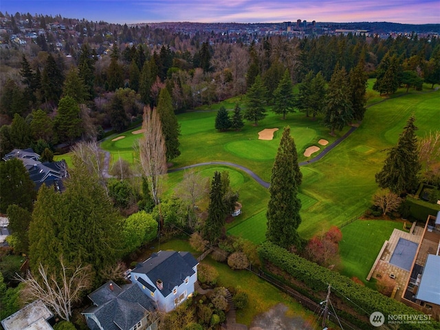 aerial view at dusk with golf course view and a view of trees