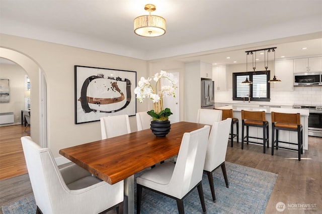 dining area featuring recessed lighting, arched walkways, dark wood-style flooring, and radiator heating unit