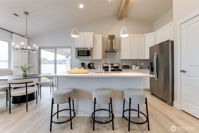 kitchen featuring vaulted ceiling with beams, visible vents, appliances with stainless steel finishes, a sink, and wall chimney exhaust hood